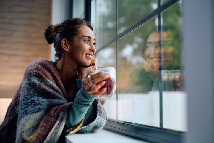 Smiling woman day dreaming while drinking warm tea at home