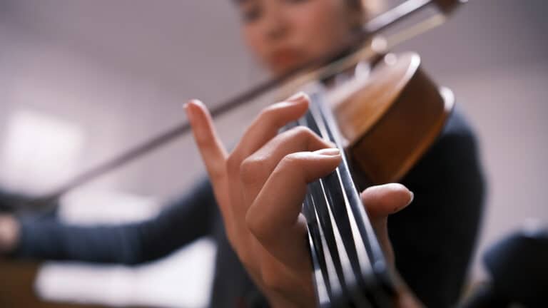 Close-up of a violinist's fingers healing chords on the strings of a violin. A young Asian woman plays the violin, the focus is on her hand. Music school