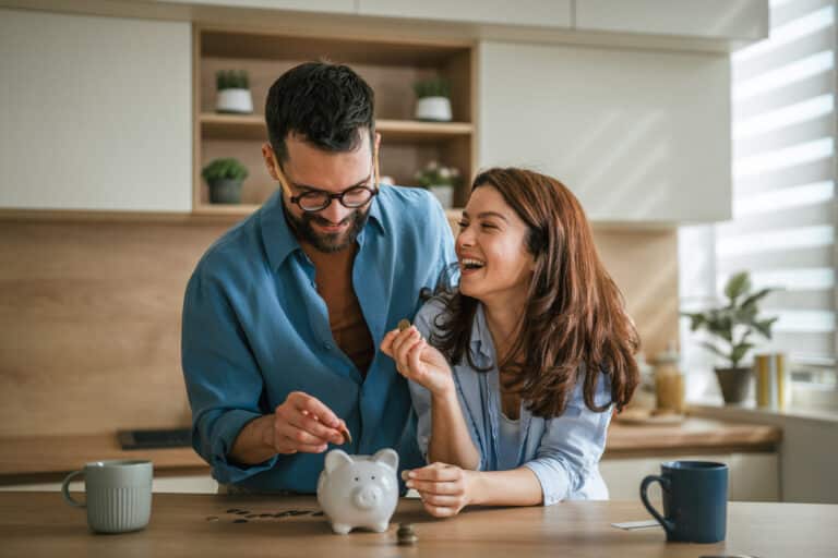 Happy couple saving money in piggy bank at home kitchen